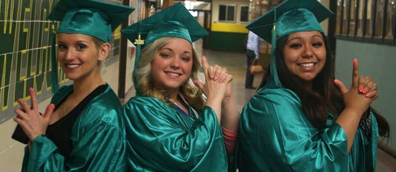 Three First Institute Graduates in full cap and gown in a Charlie's Angels pose.