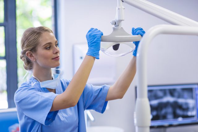 a female dental assistant is adjusting dental equipment